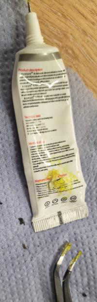 Tube of half empty yellow glue with a rift in the bottom half with black tweezers beneath